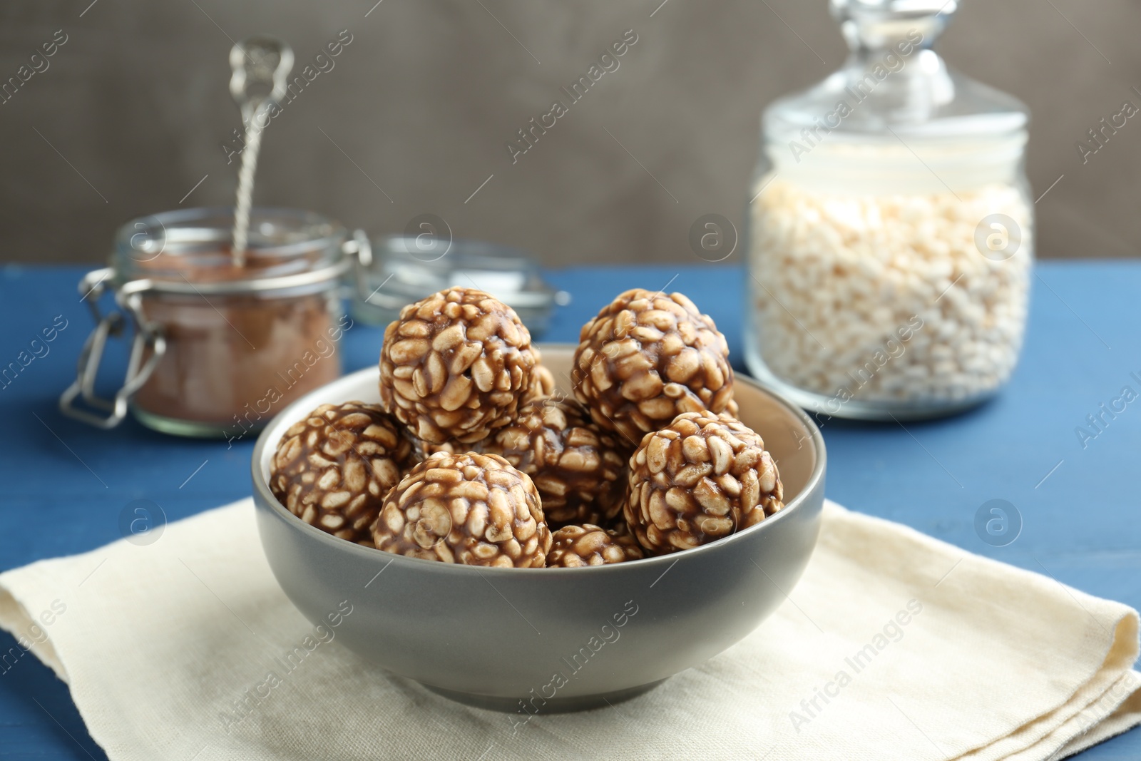 Photo of Tasty chocolate puffed rice balls in bowl on blue table, closeup