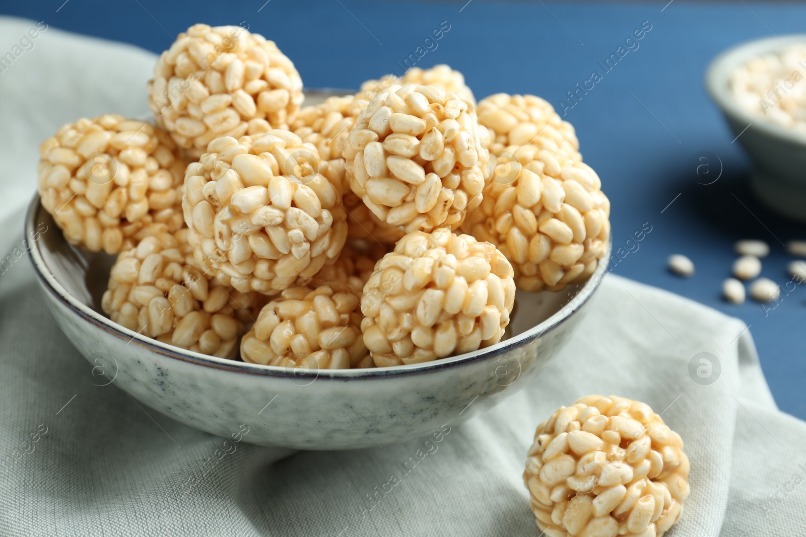 Photo of Tasty puffed rice balls in bowl on blue table, closeup