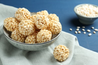 Tasty puffed rice balls in bowl on blue table, closeup