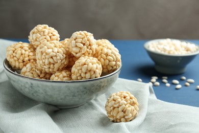 Photo of Tasty puffed rice balls in bowl on blue table, closeup