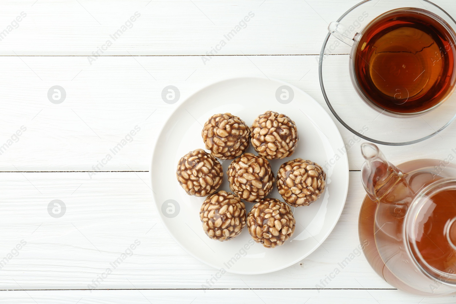 Photo of Tasty chocolate puffed rice balls and tea on white wooden table, flat lay. Space for text