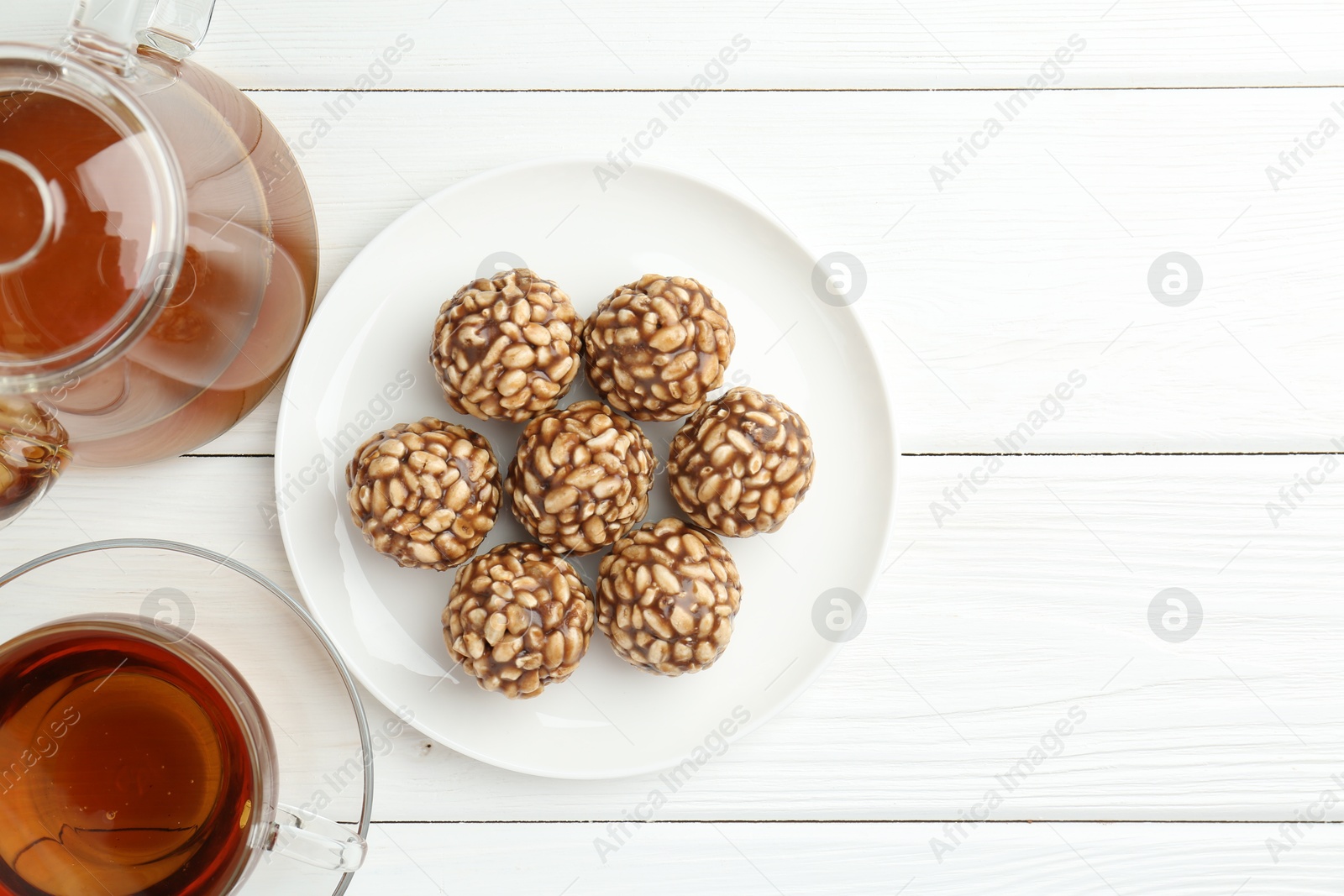 Photo of Tasty chocolate puffed rice balls and tea on white wooden table, flat lay. Space for text