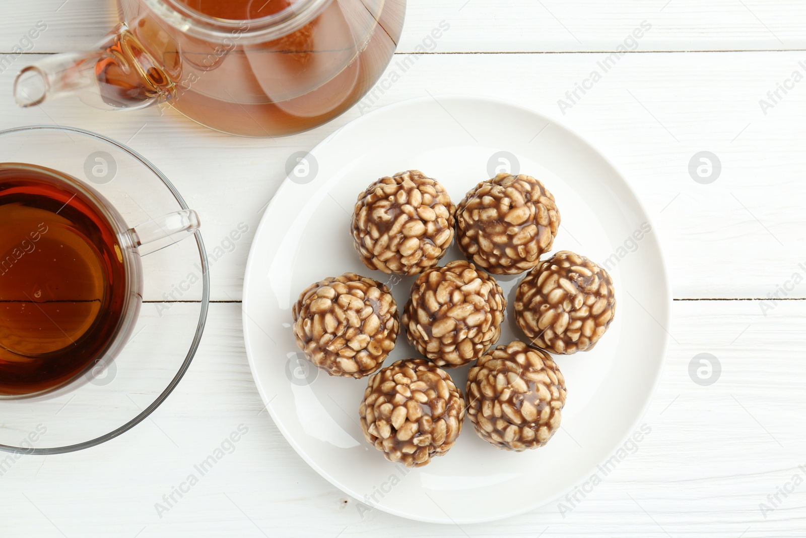 Photo of Tasty chocolate puffed rice balls and tea on white wooden table, flat lay