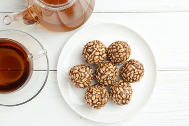 Photo of Tasty chocolate puffed rice balls and tea on white wooden table, flat lay