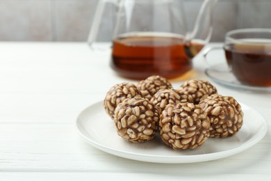 Photo of Tasty chocolate puffed rice balls and tea on white wooden table, closeup. Space for text