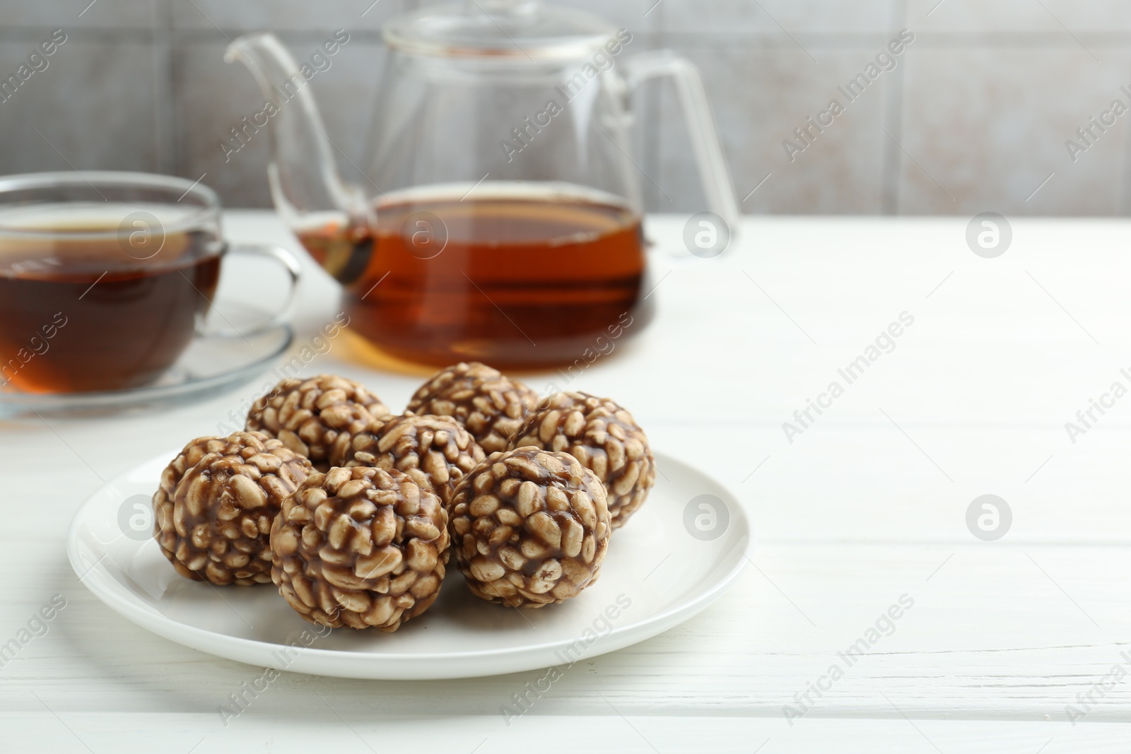 Photo of Tasty chocolate puffed rice balls and tea on white wooden table, closeup. Space for text