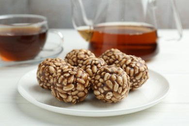 Photo of Tasty chocolate puffed rice balls and tea on white wooden table, closeup