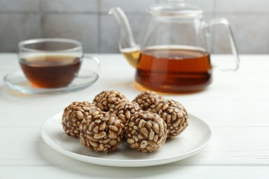 Photo of Tasty chocolate puffed rice balls and tea on white wooden table, closeup