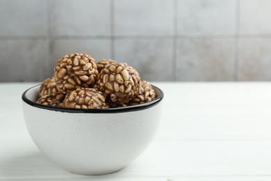 Photo of Tasty chocolate puffed rice balls in bowl on white wooden table, closeup. Space for text