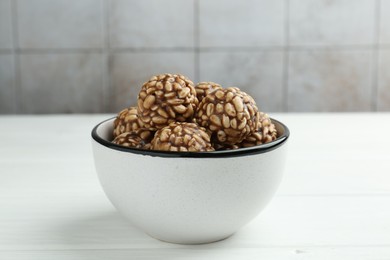 Photo of Tasty chocolate puffed rice balls in bowl on white wooden table, closeup