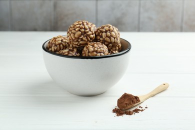 Tasty chocolate puffed rice balls in bowl and cocoa powder on white wooden table