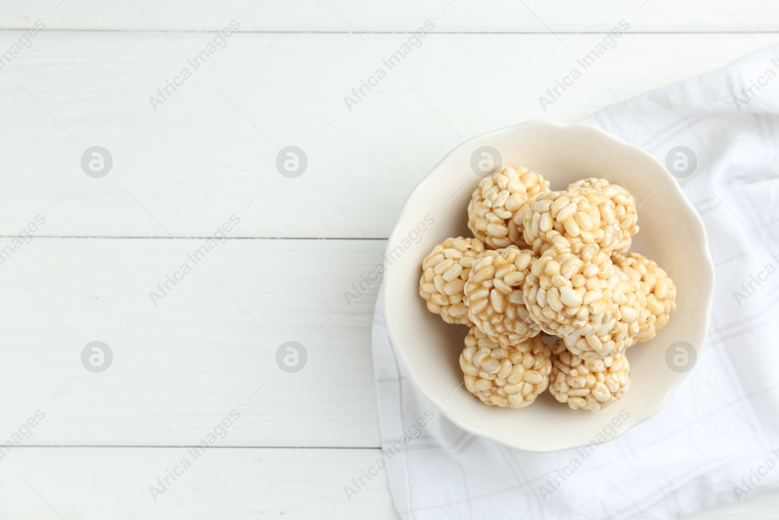 Photo of Tasty puffed rice balls in bowl on white wooden table, top view. Space for text