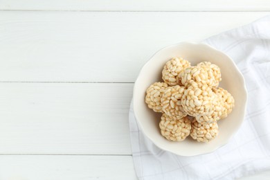 Tasty puffed rice balls in bowl on white wooden table, top view. Space for text