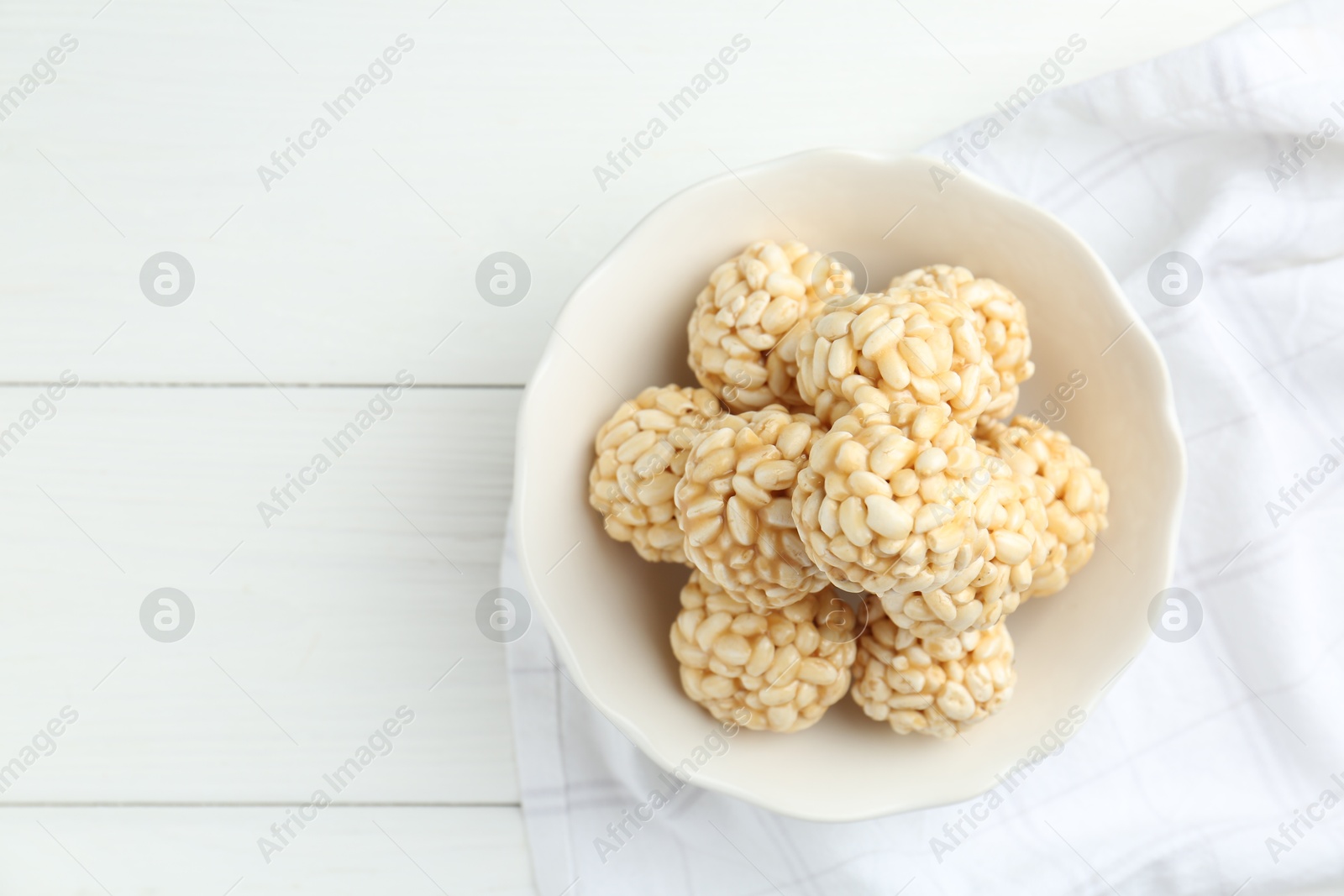 Photo of Tasty puffed rice balls in bowl on white wooden table, top view. Space for text