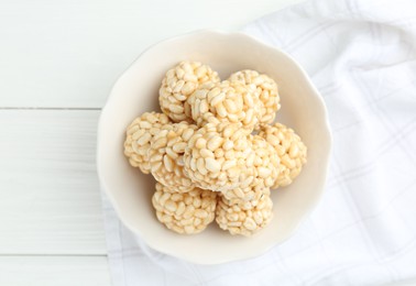 Tasty puffed rice balls in bowl on white wooden table, top view