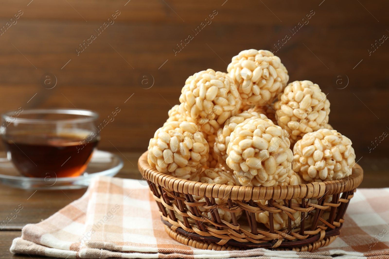 Photo of Tasty puffed rice balls in wicker basket and tea on wooden table, closeup