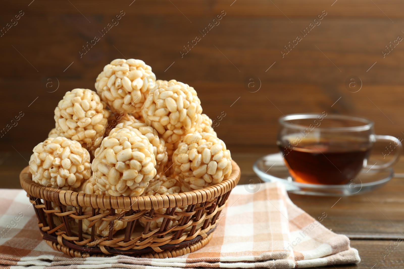 Photo of Tasty puffed rice balls in wicker basket and tea on wooden table, closeup