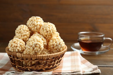 Tasty puffed rice balls in wicker basket and tea on wooden table, closeup