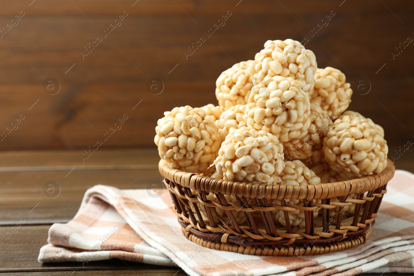 Photo of Tasty puffed rice balls in wicker basket on wooden table, space for text