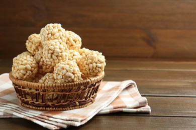 Photo of Tasty puffed rice balls in wicker basket on wooden table, space for text