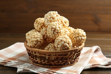 Tasty puffed rice balls in wicker basket on wooden table, closeup