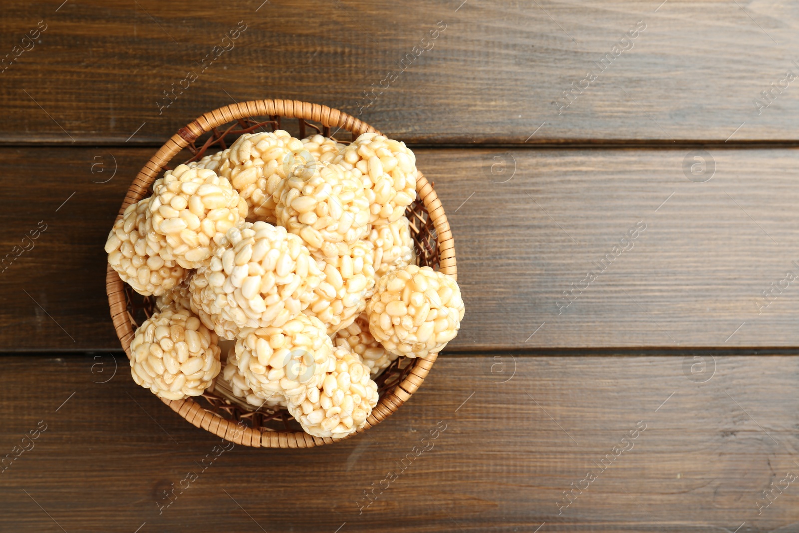 Photo of Tasty puffed rice balls in wicker basket on wooden table, top view. Space for text