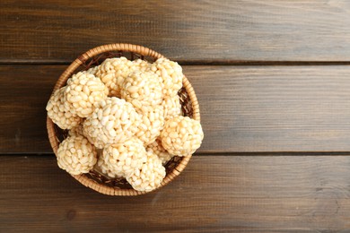 Photo of Tasty puffed rice balls in wicker basket on wooden table, top view. Space for text