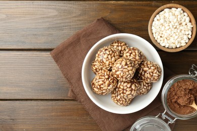 Photo of Tasty chocolate puffed rice balls in bowl and ingredients on wooden table, flat lay. Space for text