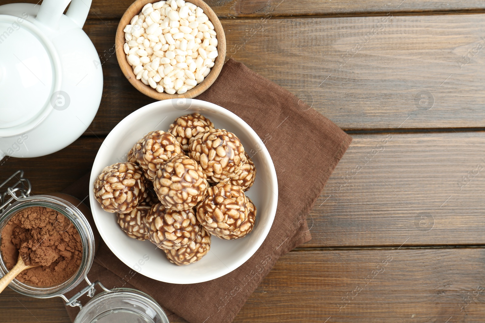 Photo of Tasty chocolate puffed rice balls, ingredients and teapot on wooden table, flat lay. Space for text