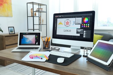 Designer's workplace with computer, tablet, laptop, color palettes and stationery on wooden table indoors