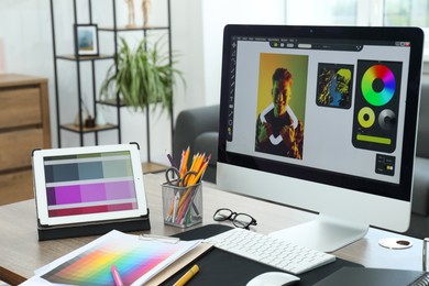 Photo of Designer's workplace with computer, tablet, color palettes and stationery on wooden table indoors