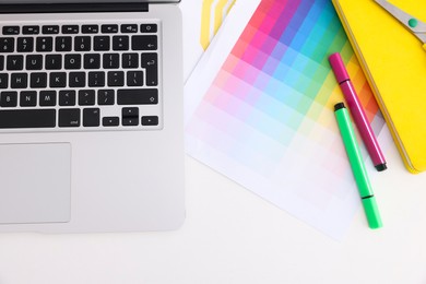 Photo of Designer's workplace with laptop, color palette and stationery on white table, flat lay