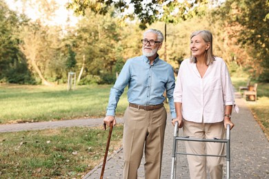 Senior couple with walking frame and cane in park, space for text