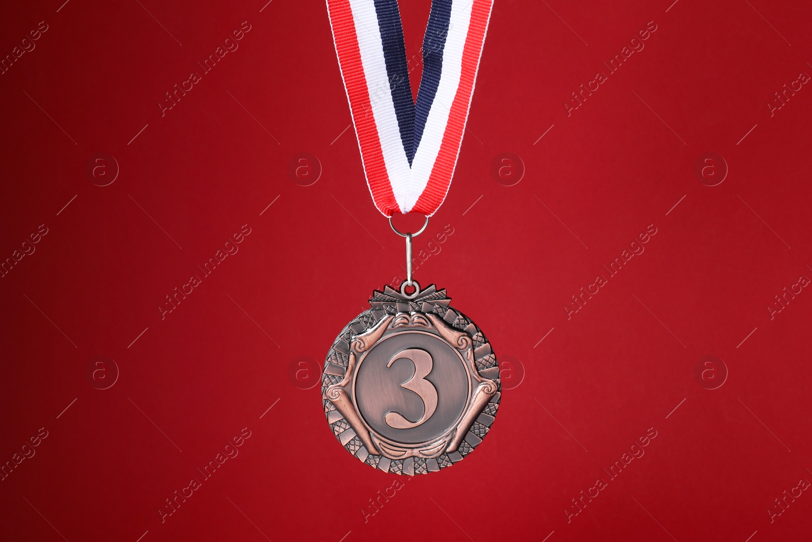 Photo of Bronze medal with striped ribbon on red background