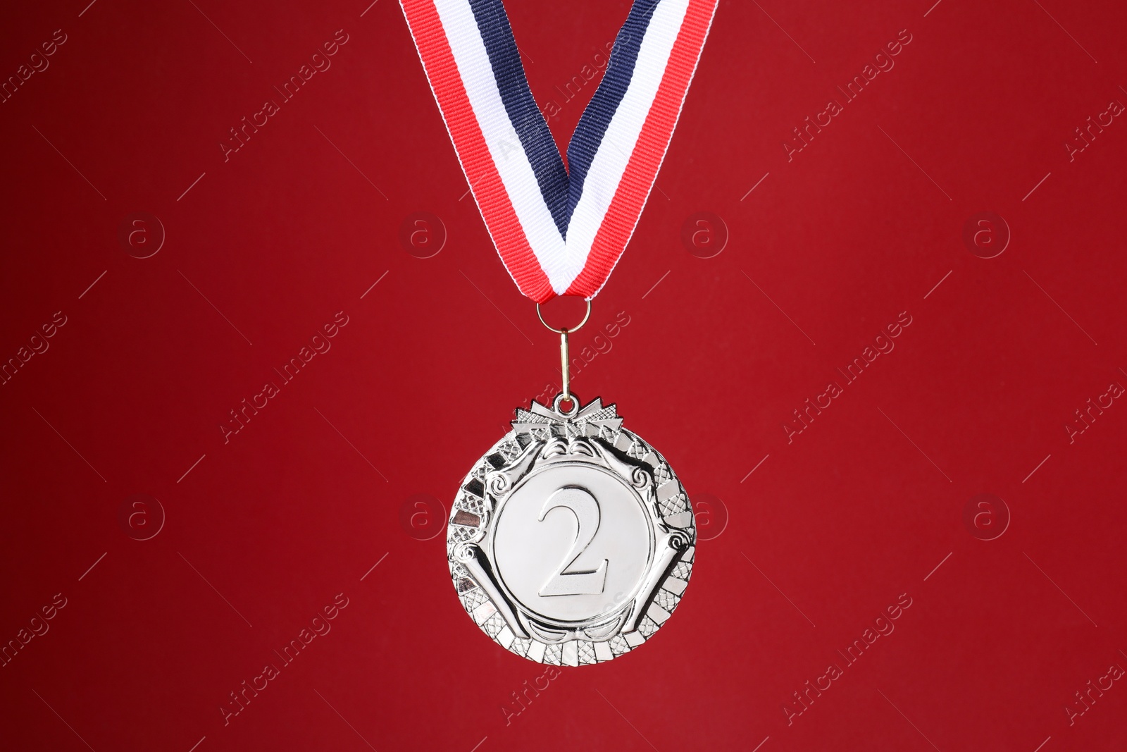 Photo of Silver medal with striped ribbon on red background