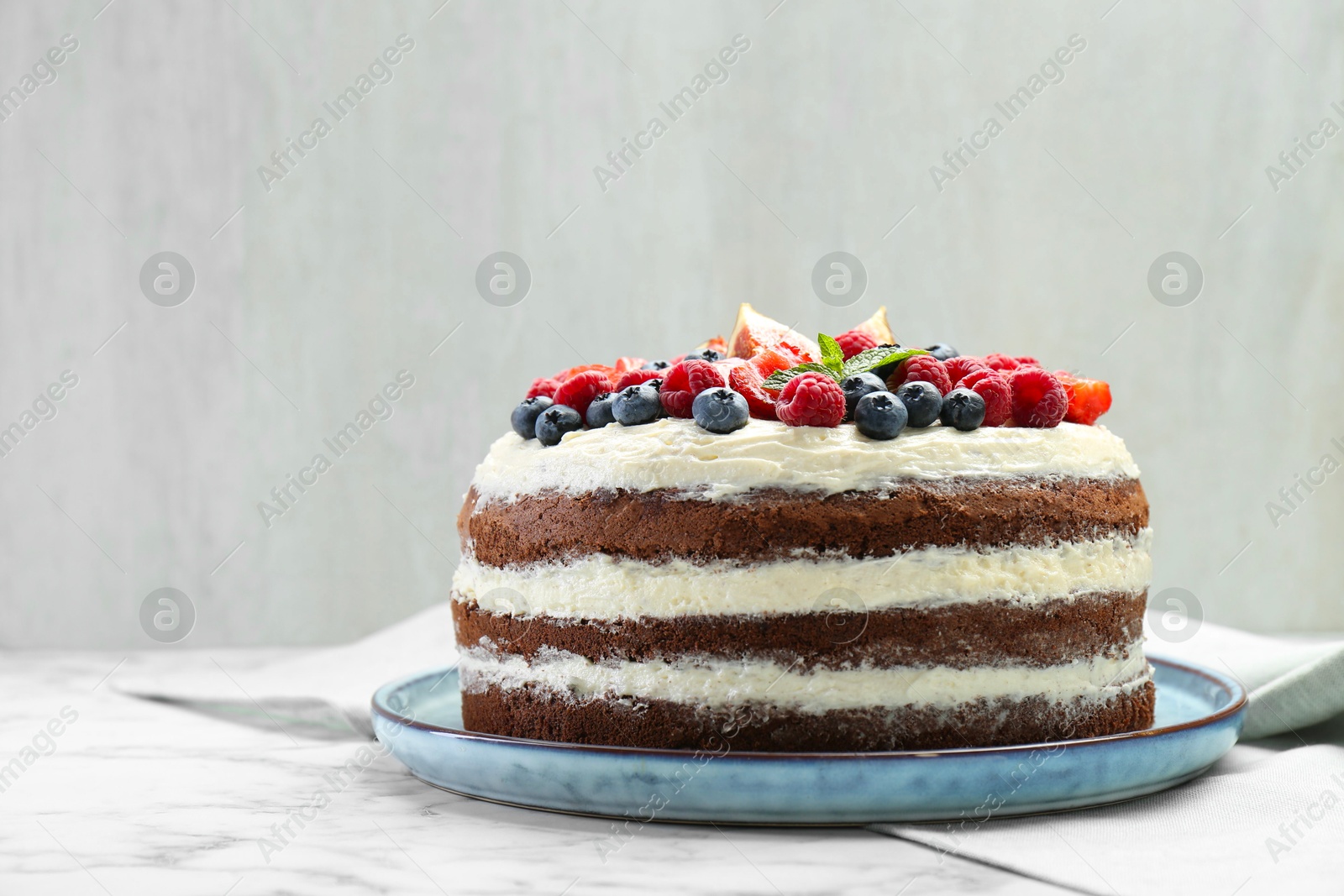 Photo of Delicious chocolate sponge cake with berries on white marble table