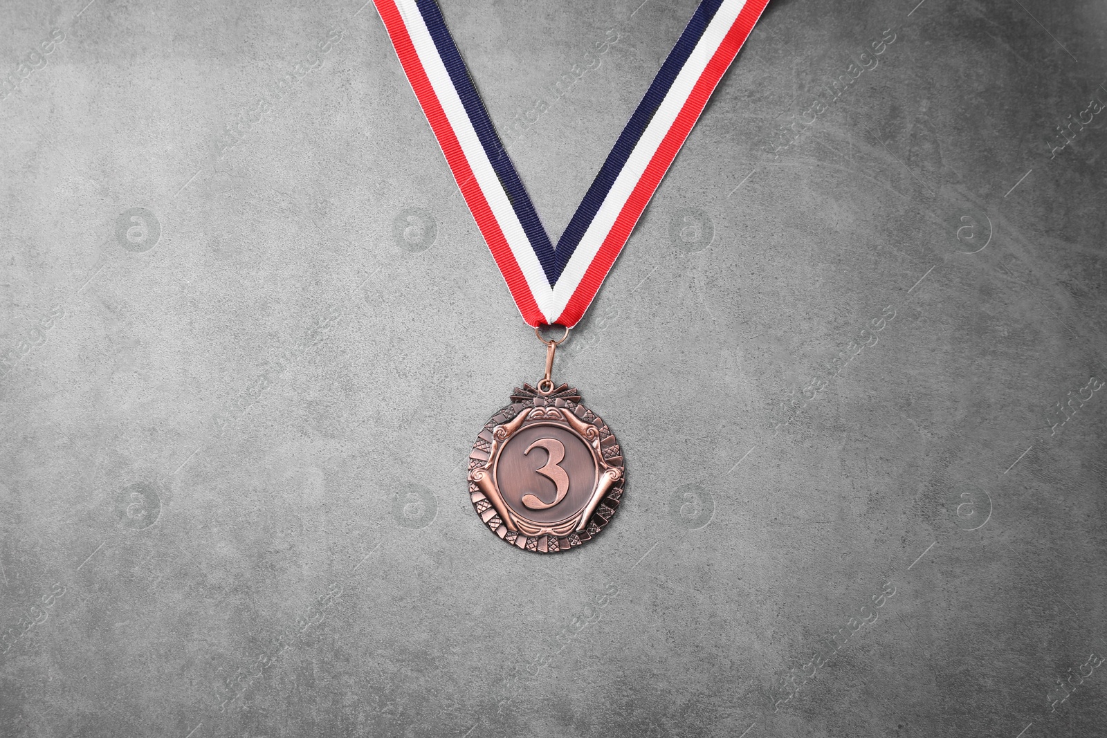 Photo of Bronze medal with striped ribbon on grey background, top view