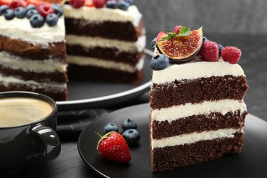 Piece of delicious chocolate sponge cake with berries and coffee on black table, closeup