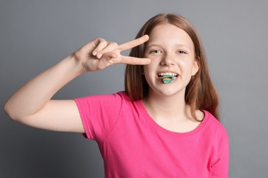 Photo of Teenage girl eating tasty rainbow sour belt while showing v-sign on grey background