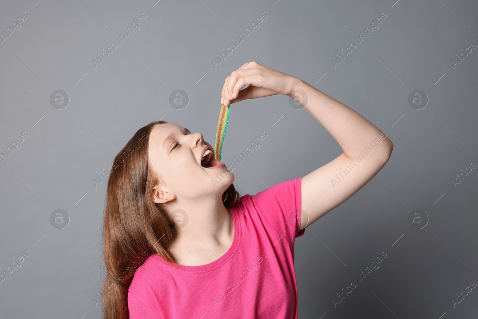 Photo of Teenage girl eating tasty rainbow sour belt on grey background