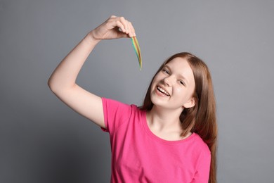 Happy teenage girl with tasty rainbow sour belt on grey background