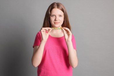 Photo of Teenage girl with tasty rainbow sour belt on grey background