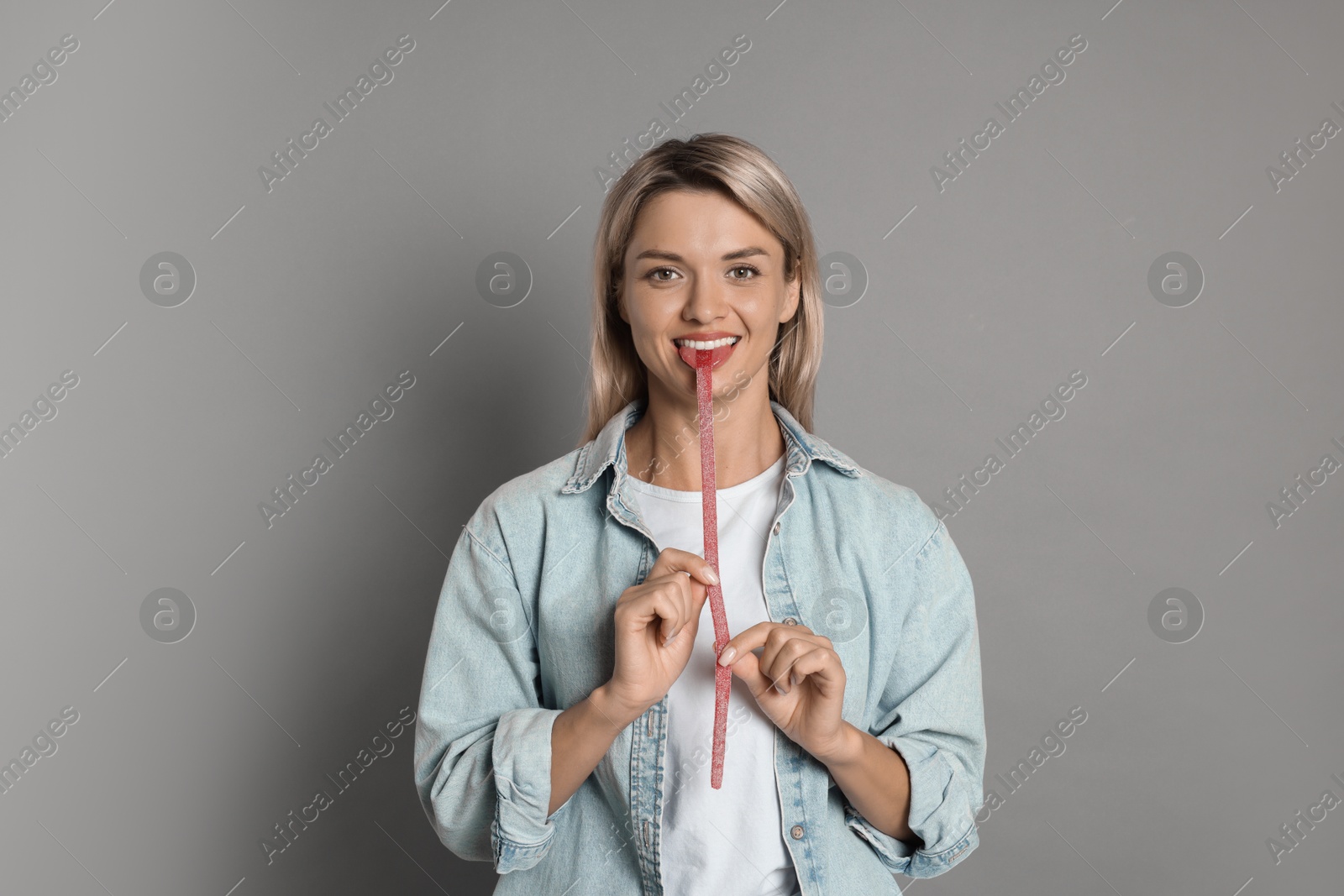 Photo of Young woman eating tasty gummy candy on grey background