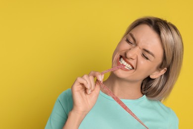 Photo of Young woman eating tasty gummy candy on yellow background