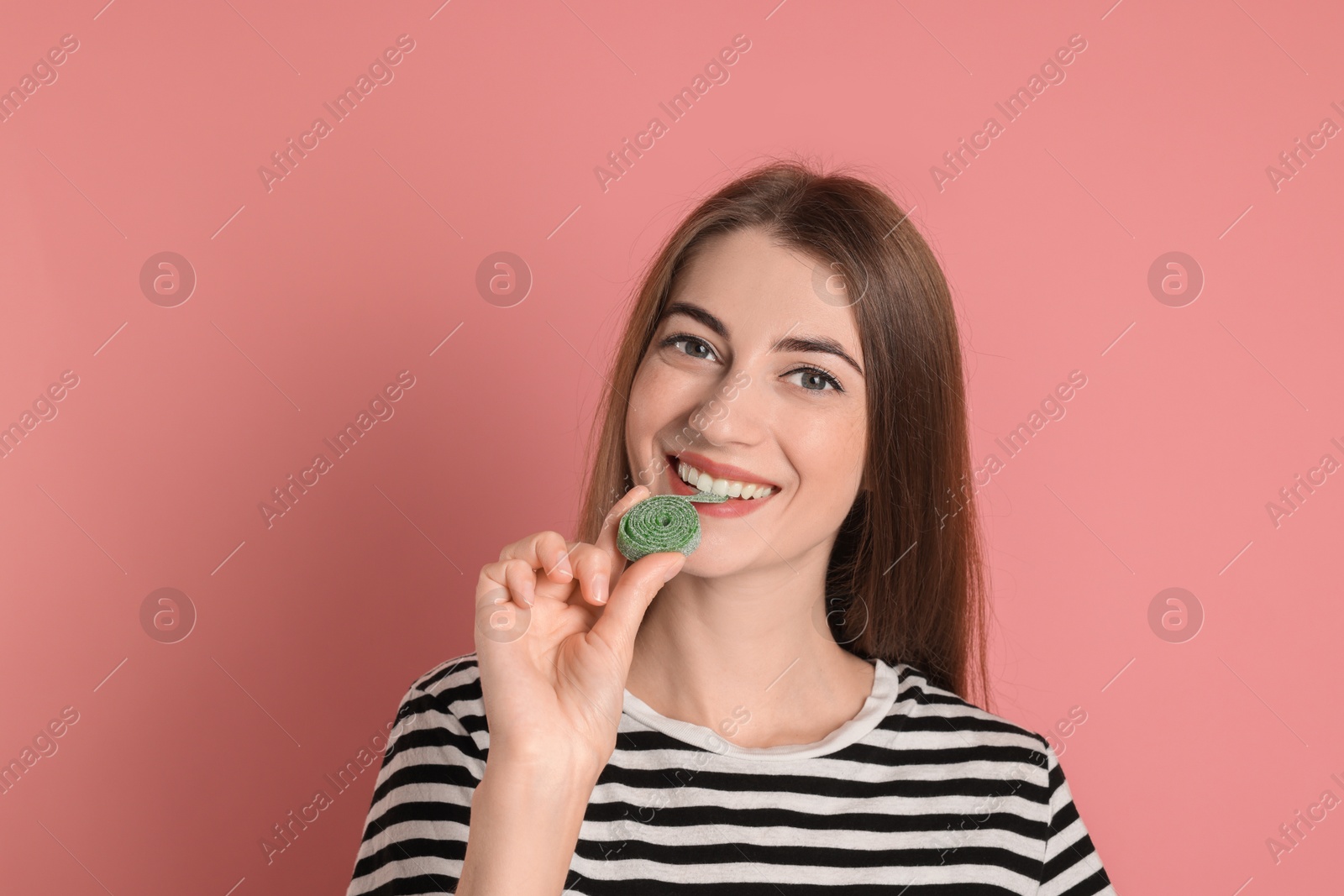 Photo of Young woman eating tasty gummy candy on pink background