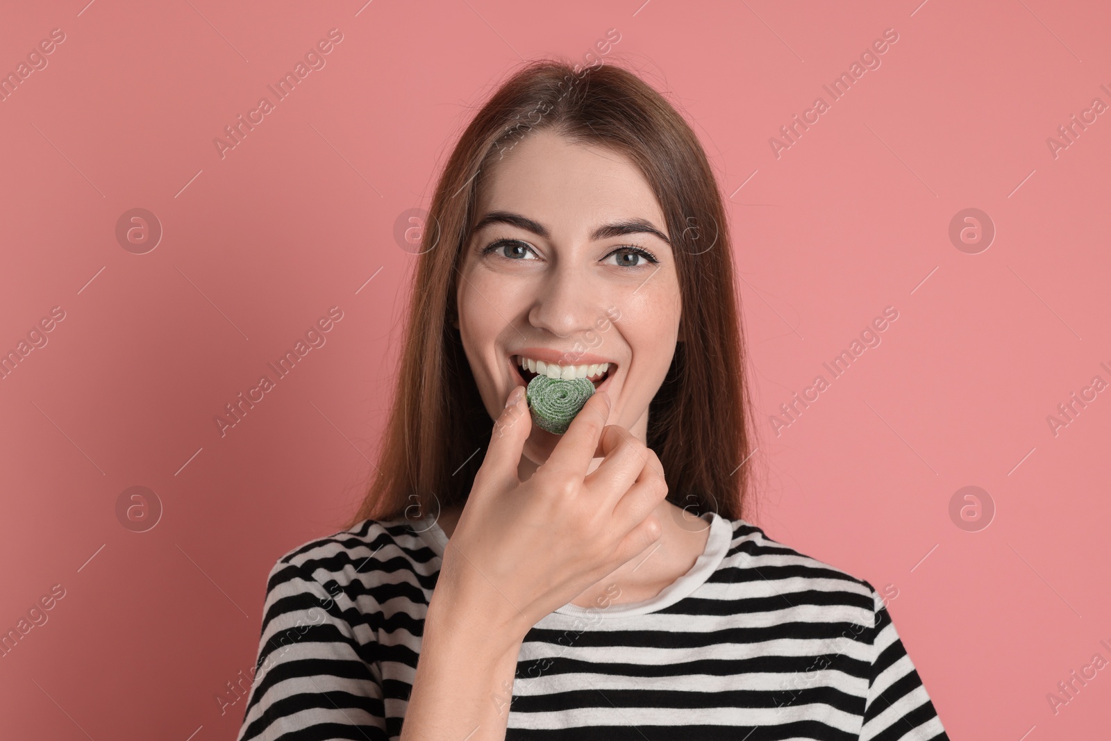 Photo of Young woman eating tasty gummy candy on pink background