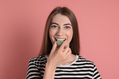 Photo of Young woman eating tasty gummy candy on pink background