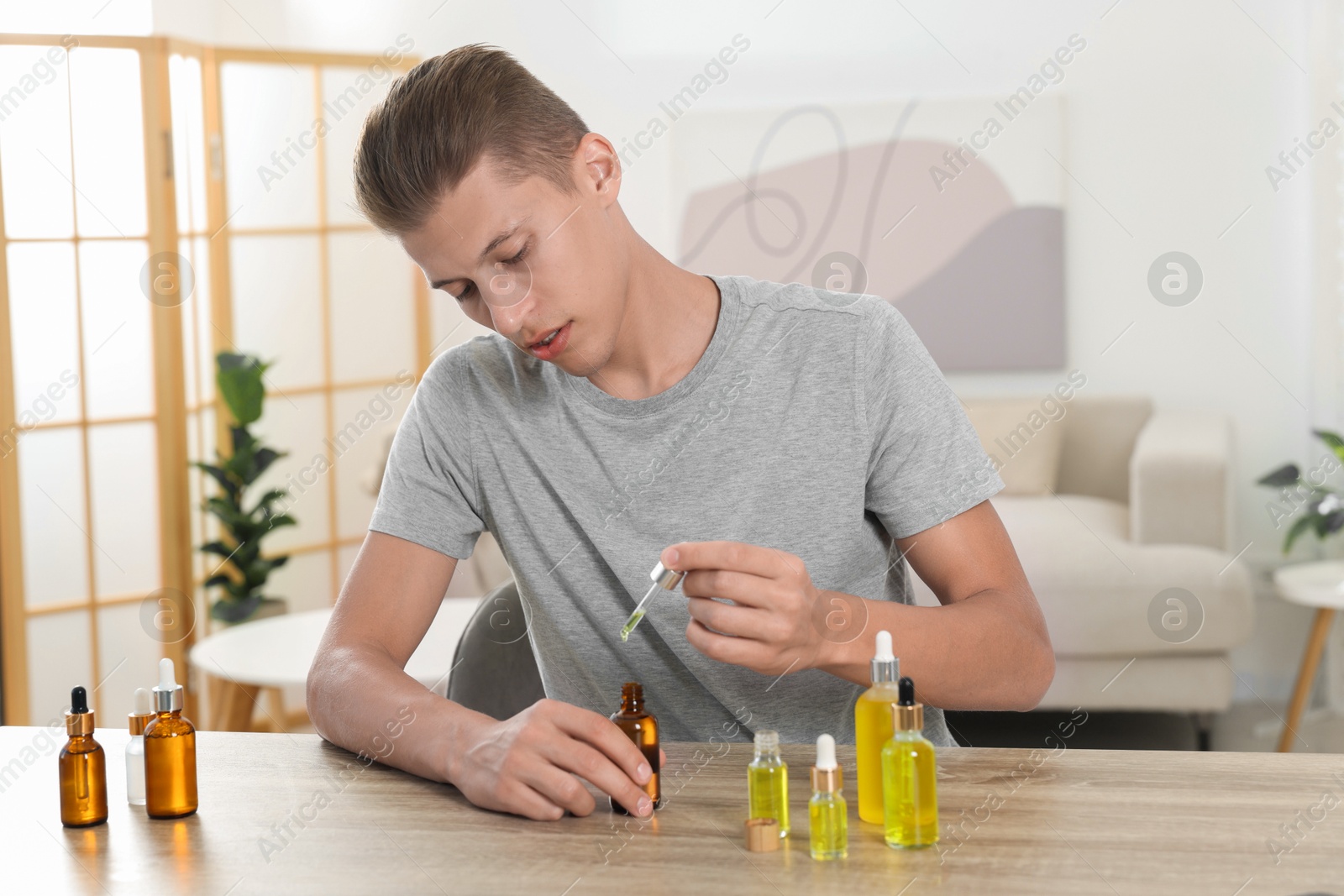 Photo of Young man dripping CBD tincture into bottle from dropper at wooden table