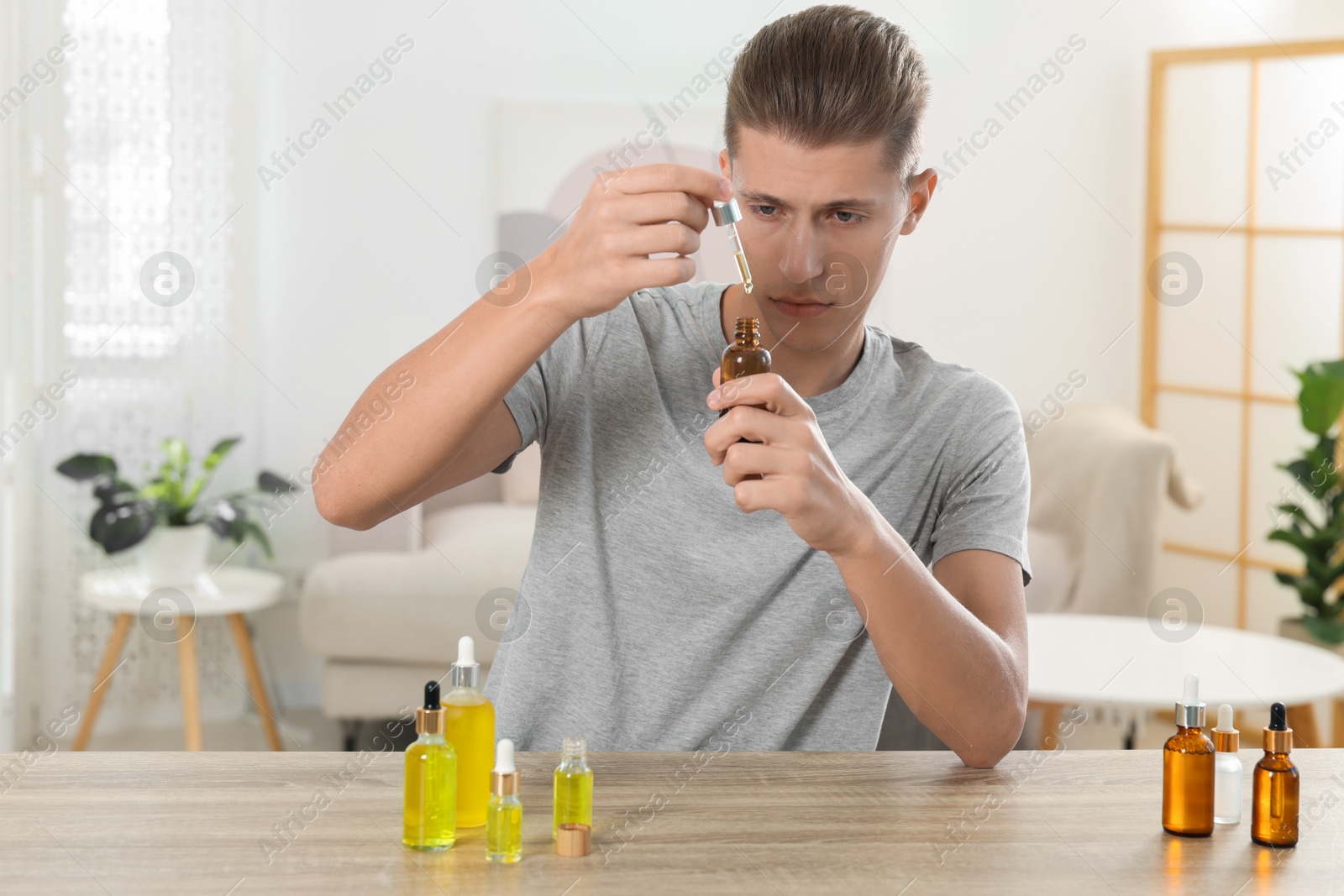 Photo of Young man dripping CBD tincture into bottle from dropper at wooden table