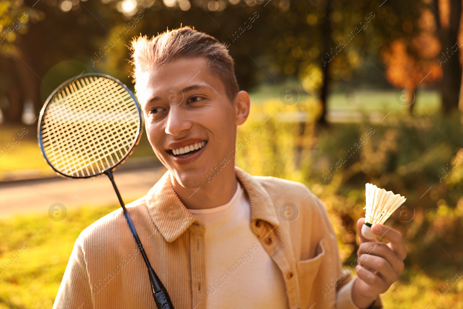 Photo of Happy young man with badminton racket and shuttlecock in park on sunny day